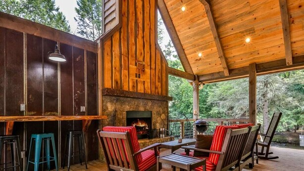 A rustic wooden cabin with a stone fireplace, wooden deck, and outdoor seating area.