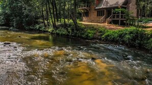 A cabin by a flowing river surrounded by dense forest.