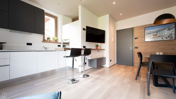 Una cocina moderna con comedor, televisor montado en la pared y puerta de madera.