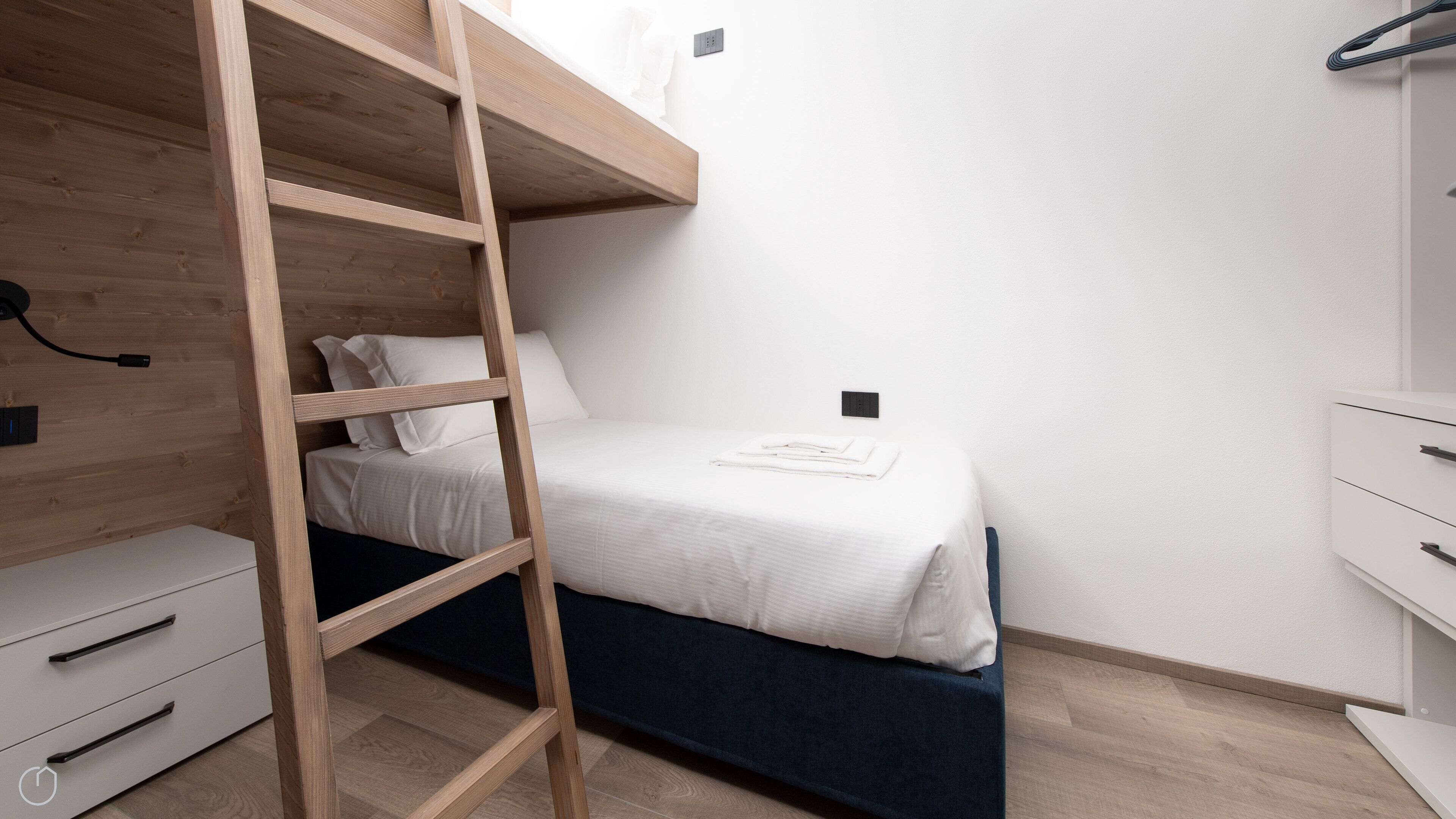 Un lit superposé avec une échelle en bois, une table de chevet blanche et une commode blanche.