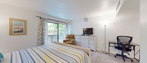 Un dormitorio con cama, cómoda, silla, escritorio, televisor y ventana con cortinas.