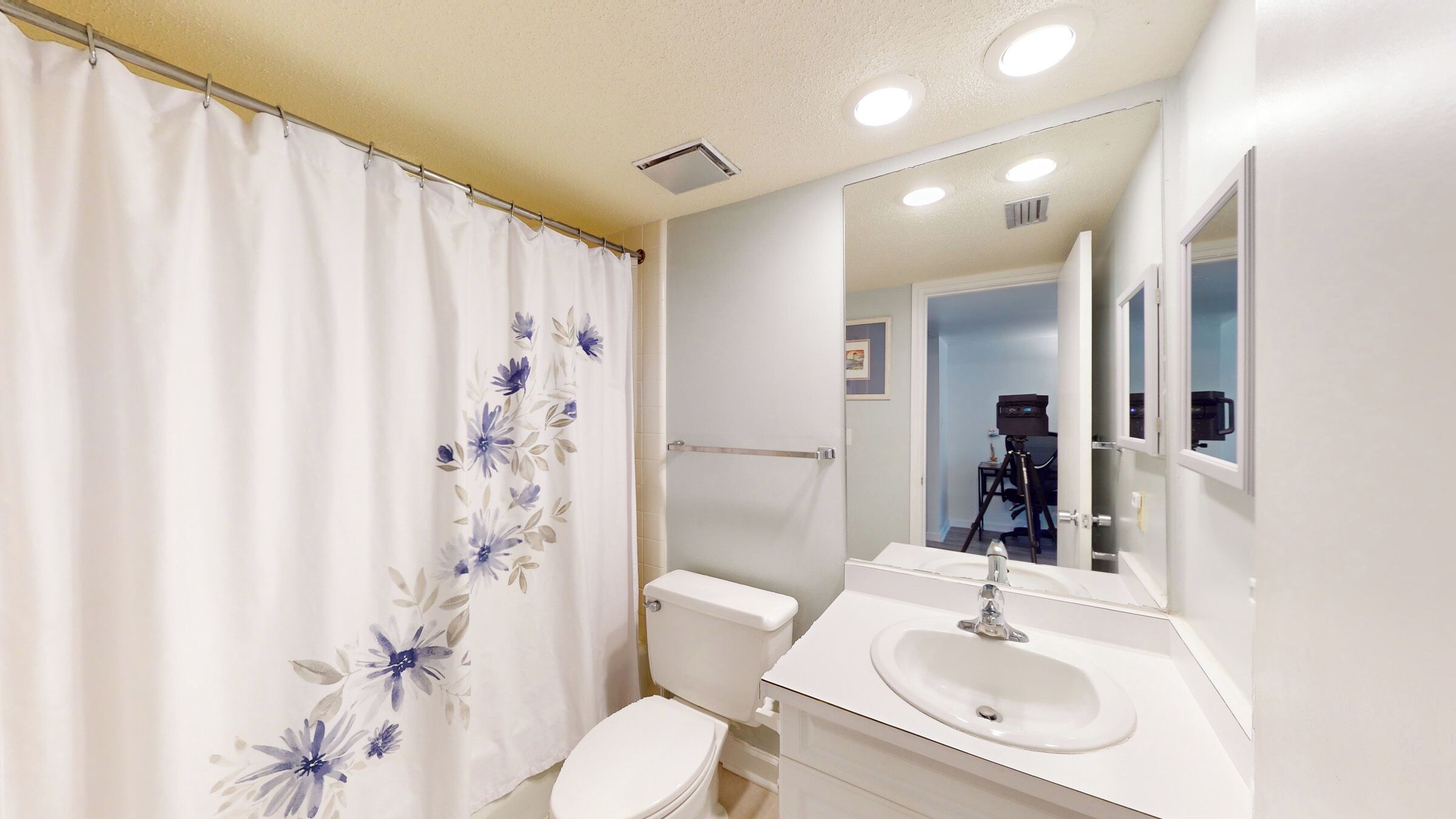 Une salle de bain équipée d’un rideau de douche, de toilettes, d’un lavabo et d’un miroir.