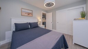 A bedroom with a bed, a bedside table, a lamp, a ceiling fan, and a door leading to a kitchen. - Lakeside Serenity: One-Bedroom Villa (Bridgman)