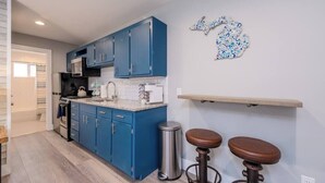A kitchen with blue cabinets, a stainless steel trash can, and two stools. - Lakeside Serenity: One-Bedroom Villa (Bridgman)
