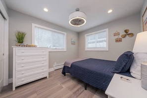 Ein Schlafzimmer mit Bett, Kommode, Fenstern, Deckenventilator und Wanddekorationen.