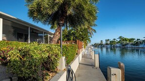A waterfront walkway with a bicycle, palm trees, and a building with large windows. - WATERFRONT!! Home w/ 37.5-ft dock, Cabana Club Membership!!! (Key Colony Beach)