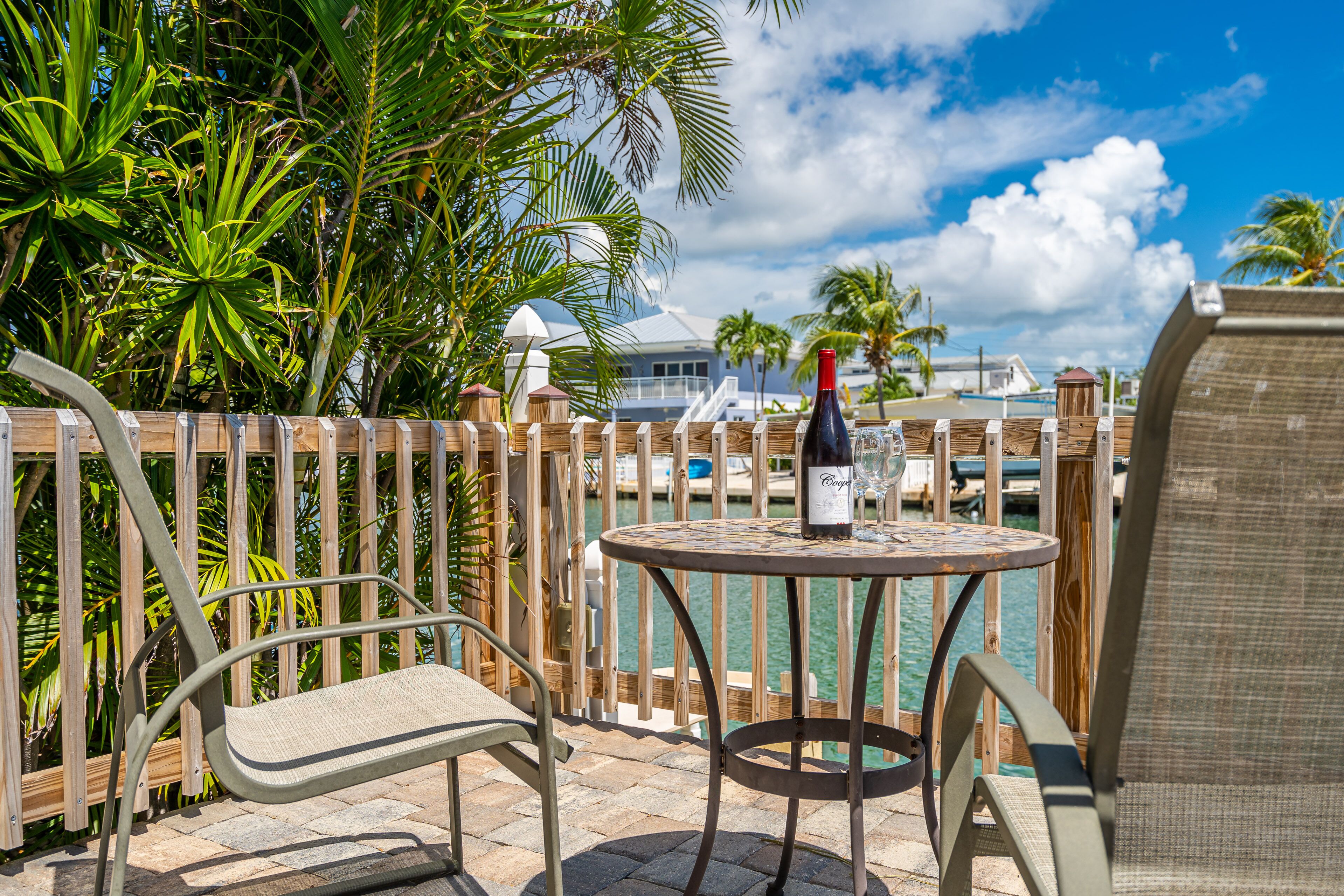 A patio with a round table, two chairs, and a bottle of wine.