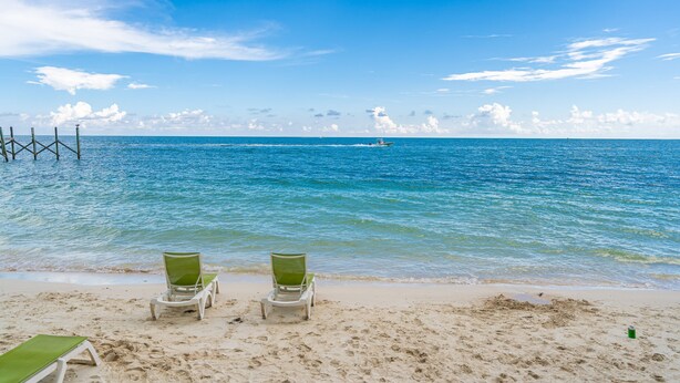 A beach with two green lounge chairs facing the ocean, a pier extending into the water, and a clear blue sky. - WATERFRONT!! Home w/ 37.5-ft dock, Cabana Club Membership!!! (Key Colony Beach)