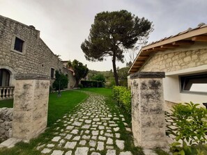 A stone pathway leading to a courtyard with a large tree and stone buildings.