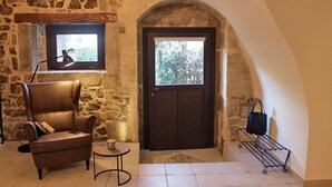 Une pièce aux murs de pierre, avec un fauteuil en cuir, une petite table, une porte et une fenêtre.
