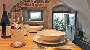 Une table à manger dressée avec une bouteille de vin, des verres et des bols, dans une pièce aux murs de pierre offrant une vue panoramique.