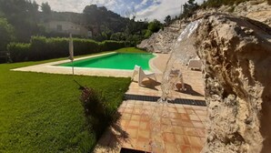 Une piscine bordée de pierres, entourée d’une pelouse bien entretenue et d’une falaise rocheuse.