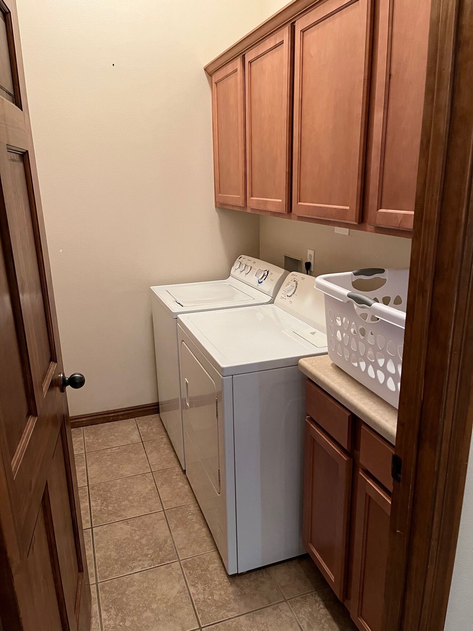 A laundry room with a front-loading washer and dryer, wooden cabinets, and a laundry basket on the countertop.