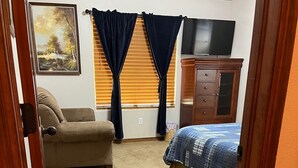 Quarto com cama, cômoda, cadeira e um quadro na parede.