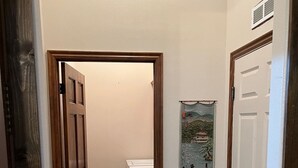 Um corredor estreito com chão de azulejos, uma máquina de lavar e uma porta com um cartaz na parede.
