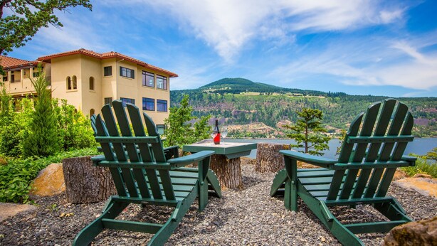 A view of a lakeside property with two Adirondack chairs, a table with a bottle, and a building with a red roof. - Luxurious Condominium 1 - 3 bedrooms available (Hood River)