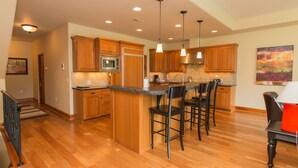 A modern kitchen with wooden cabinets, a central island, bar stools, and pendant lighting. - Luxurious Condominium 1 - 3 bedrooms available (Hood River)