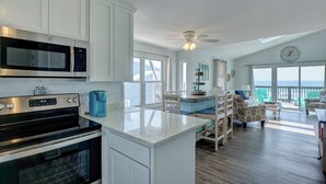 A spacious kitchen with white cabinets, a large island, and a dining area with teal chairs. - 2284-B New River Inlet Road- Direct Oceanfront 3 bedroom- Adjoining Side is Available for Rent- 2... (North Topsail Beach)