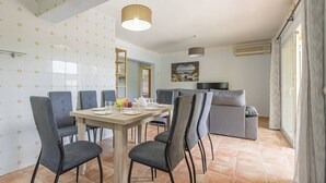 Een moderne eetruimte met een houten tafel en grijs gestoffeerde stoelen, een grijze bank en een schilderij aan de muur.