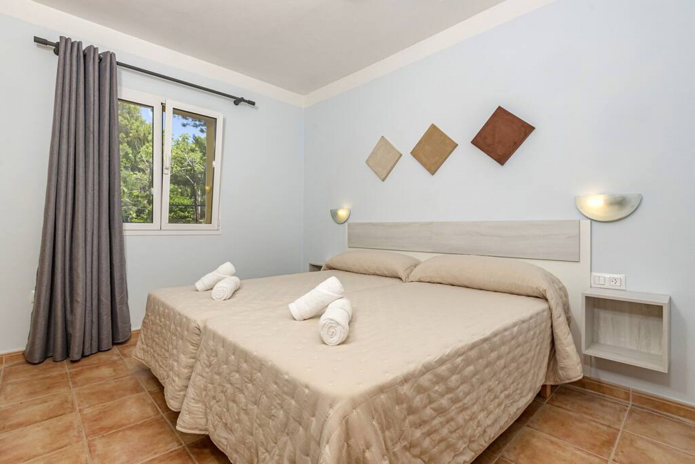 Un dormitorio con cama, cortinas, una ventana y lámparas fijadas a la pared.