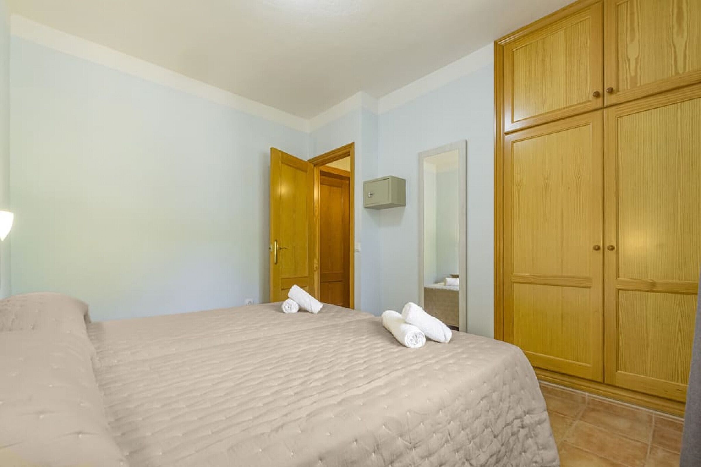 A hotel room with a bed, a wooden wardrobe, and a door leading to another room.