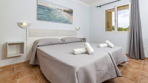 Een hotelkamer met een bed, een schilderij van een strand, een raam met gordijnen en een nachtkastje.