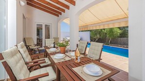 An outdoor dining area with wooden tables and chairs, a pool in the background, and a covered seating area. - Villa Astur ☀☀Charming Villa with private pool and garden (Binibequer)
