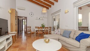 A living room with a TV, white coffee table, beige sofa, wooden dining table, and chairs. - Villa Astur ☀☀Charming Villa with private pool and garden (Binibequer)