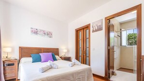 A hotel room with a bed, wooden headboard, bedside tables with lamps, a wardrobe, and a sliding glass door leading to a balcony. - Villa Astur ☀☀Charming Villa with private pool and garden (Binibequer)