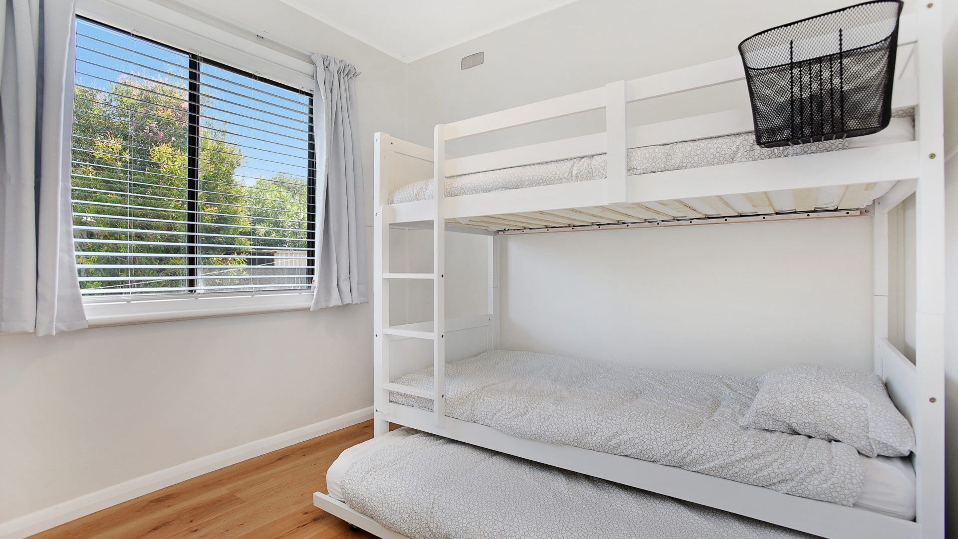 A bunk bed room with a window, a white ceiling, and a wooden floor.