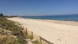 A wide sandy beach with a wooden fence on one side and a clear blue sky. - Scenic Shack - 4 Scenic Way (CARRICKALINGA)