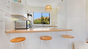 A modern kitchen with a large window, a built-in stove, and three wooden stools. - Scenic Shack - 4 Scenic Way (CARRICKALINGA)