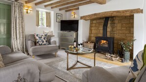 A cozy living room with a fireplace, comfortable seating, and a television. - Attractive thatched roof property in the idyllic Cotswold village of Ebrington. (Ebrington, near Chipping Campden)