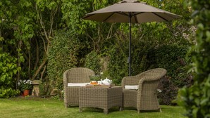 A wicker outdoor seating area with a table and chairs, an umbrella, and a potted plant. - Attractive thatched roof property in the idyllic Cotswold village of Ebrington. (Ebrington, near Chipping Campden)