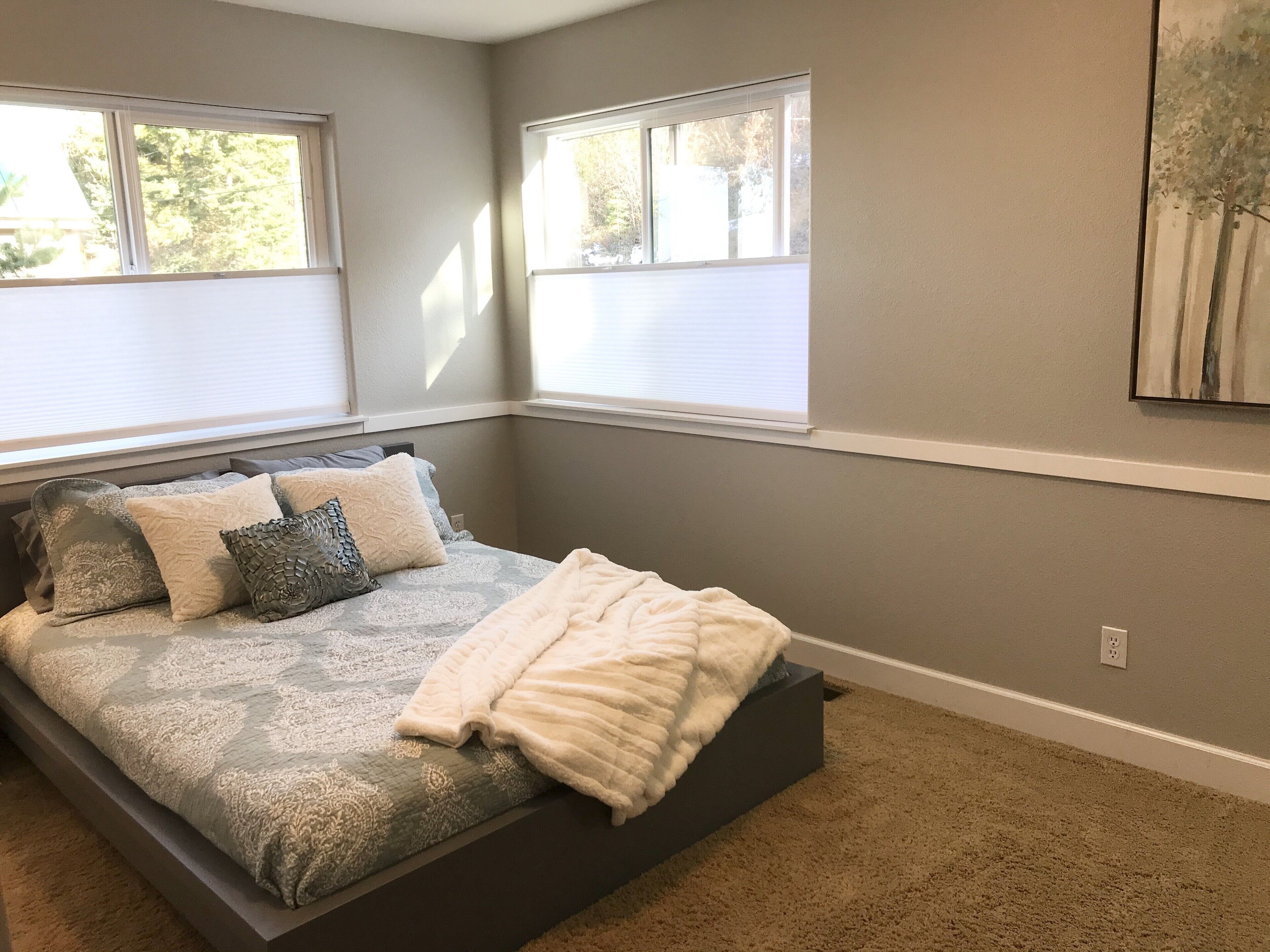 A bedroom with a bed, a window, and a painting on the wall.