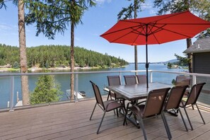 A deck with a table and chairs, overlooking a lake with a forested shore and a boat dock.