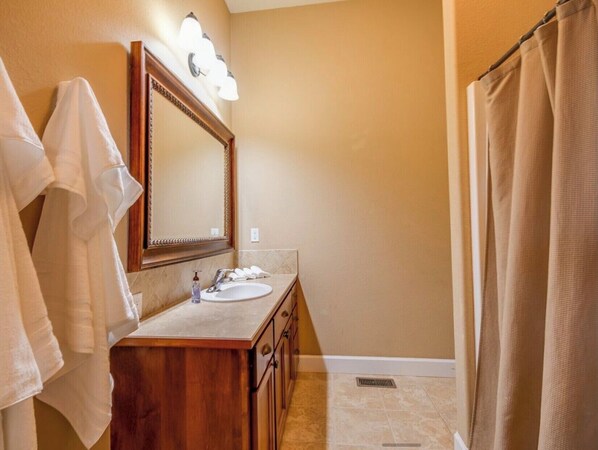 A bathroom with a wooden vanity, a large mirror, a sink, and a shower curtain. - Kidd Island (CDA) Lakefront Beauty-Amazing views! (Coeur d'Alene)