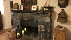 Una chimenea de piedra con un manto que exhibe diversos objetos, como un letrero enmarcado, un modelo de barco y una cabeza de ciervo.