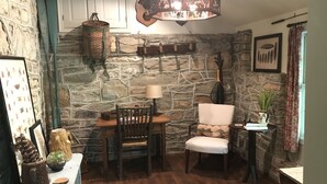 Una habitación rústica con paredes de piedra, una mesa de madera, dos sillas, un farol colgante y un cuadro enmarcado en la pared.