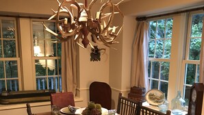Un comedor con una mesa de madera dispuesta para seis personas, rodeada de sillas. Un candelabro con adornos similares a astas cuelga del techo.