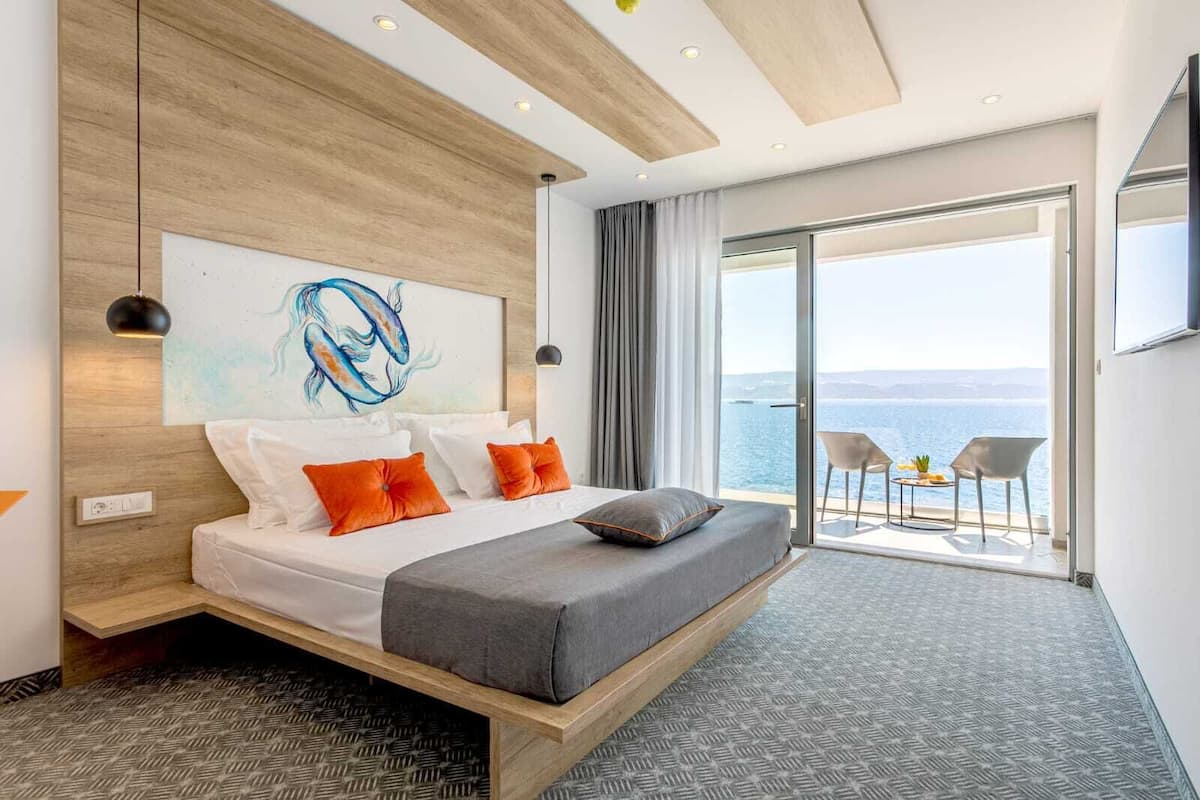 Ein modernes Hotelzimmer mit einem großen Bett, einem Gemälde und einem Balkon mit Meerblick.