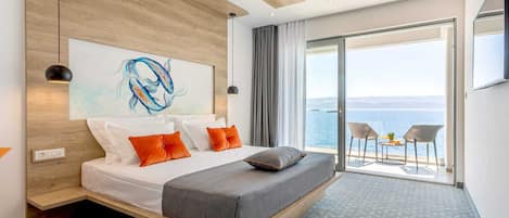 A modern hotel room with a large bed, a painting, and a balcony with a view of the sea.