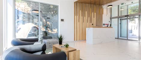 Una moderna zona de recepción con un mostrador de madera, sillas negras y un suelo de mármol.