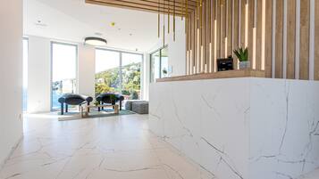 A modern reception area with a marble floor, wooden reception desk, and large windows offering a view of the outdoors.