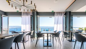 Un comedor moderno con vistas al mar, que presenta una mesa central con sillas, ventanas amplias y una lámpara de techo singular.