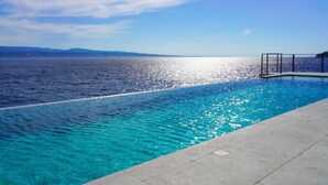 Una piscina con agua azul cristalina y vistas al mar y montañas lejanas.