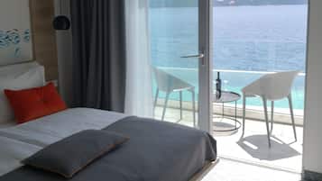 Habitación de hotel moderna con una cama, vistas al mar y un balcón con dos sillas.
