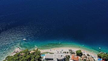 An aerial view of a coastal area with a beach, clear waters, and buildings.