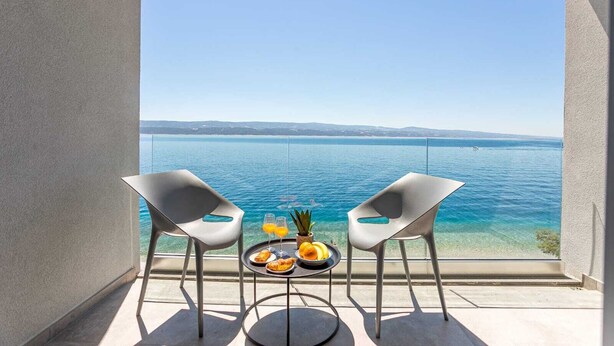 Un balcón con dos sillas y una mesa, con vista a una masa de agua y una costa distante.