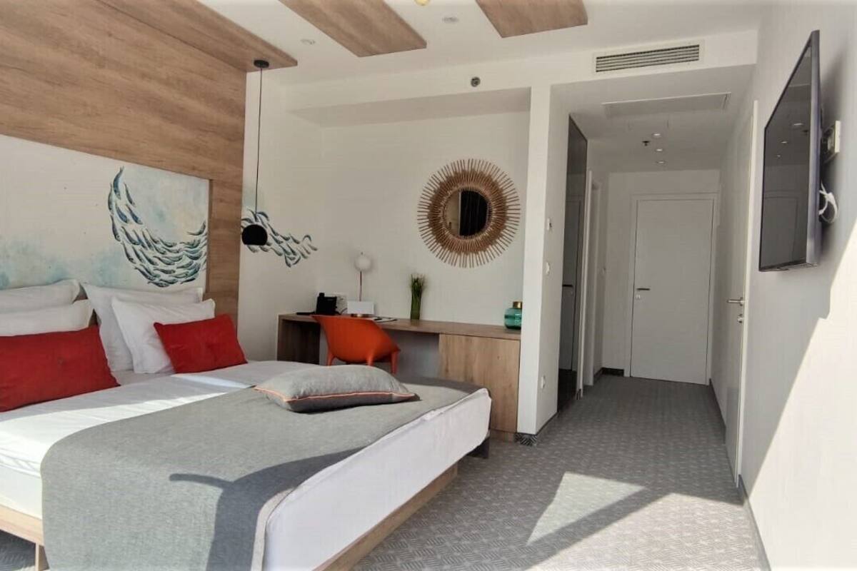 Ein modernes Schlafzimmer mit Bett, Schreibtisch, Sessel, Fernseher und einem Flur.